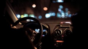 夜の車内。ステアリングとダッシュボード越しに、街の灯りがにじんで見える