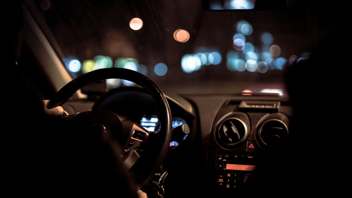 夜の車内。ステアリングとダッシュボード越しに、街の灯りがにじんで見える