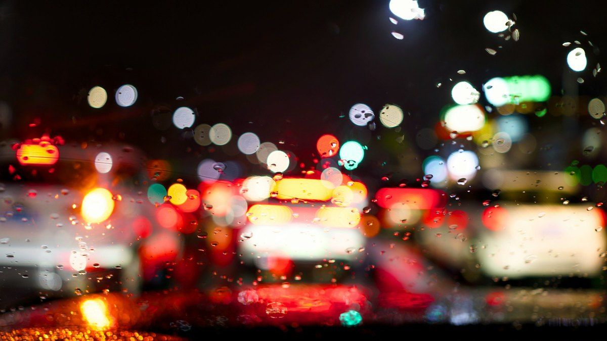 夜の車内から見た、雨粒のついたフロントガラス越しの街の灯り
