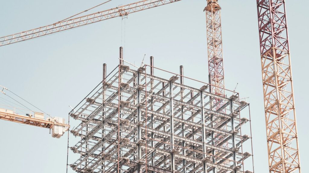 クレーンに囲まれて組み上がる建設中の鉄骨