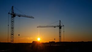 夕焼け空を背景に、建設中の現場に立つ2基のタワークレーンのシルエット