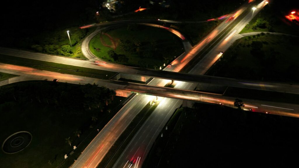 夜の高速道路のインターチェンジを上空から見た写真。分かれていく道路に車のライトの軌跡が伸びている
