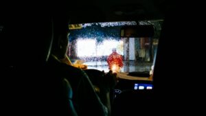 夜の雨の中、運転席からフロントガラス越しに街の明かりを見ている運転手の後ろ姿