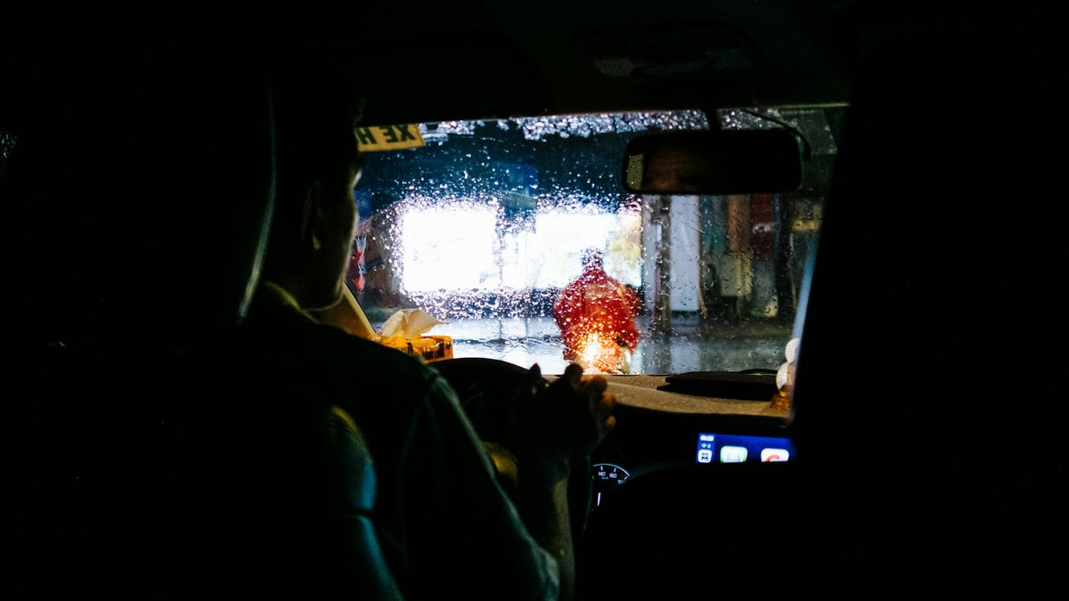 夜の雨の中、運転席からフロントガラス越しに街の明かりを見ている運転手の後ろ姿