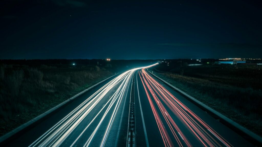 夜の高速道路を車のライトが光の帯になって流れる長時間露光の写真。トラックドライバーの夜間の長時間運行を表すイメージ