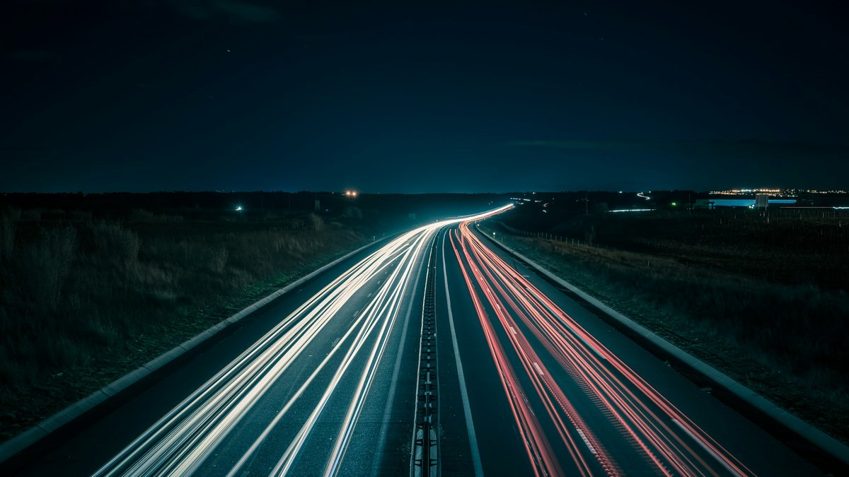 夜の高速道路を車のライトが光の帯になって流れる長時間露光の写真。トラックドライバーの夜間の長時間運行を表すイメージ