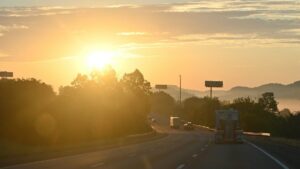 夜勤明けの高速道路に昇る朝日と走行するトラック