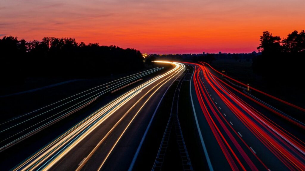 夜明けの空の下で車のライトが流れる高速道路