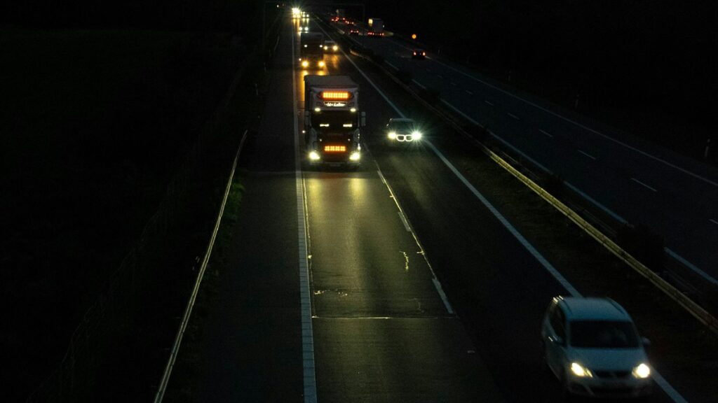 夜間の高速道路を走るトラックと乗用車。ヘッドライトが路面を照らしている