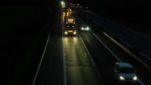 夜間の高速道路を走るトラックと乗用車。ヘッドライトが路面を照らしている