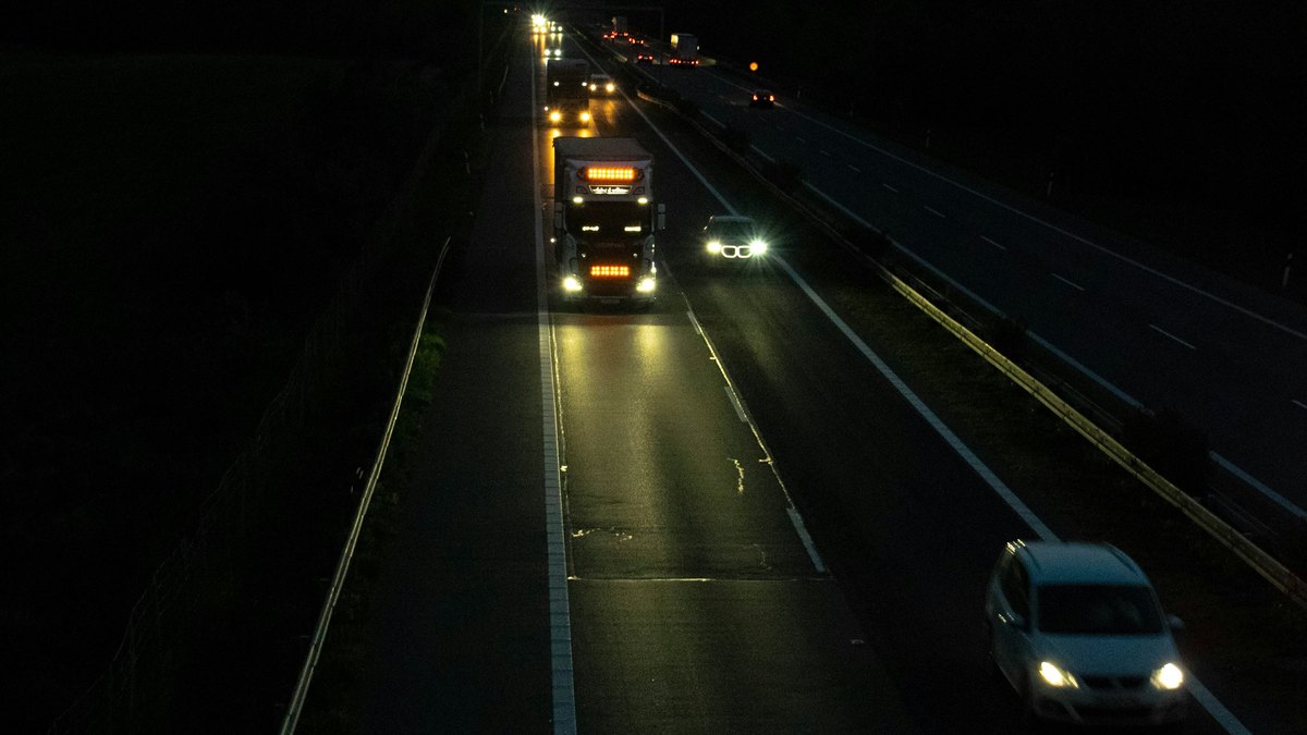 夜間の高速道路を走るトラックと乗用車。ヘッドライトが路面を照らしている
